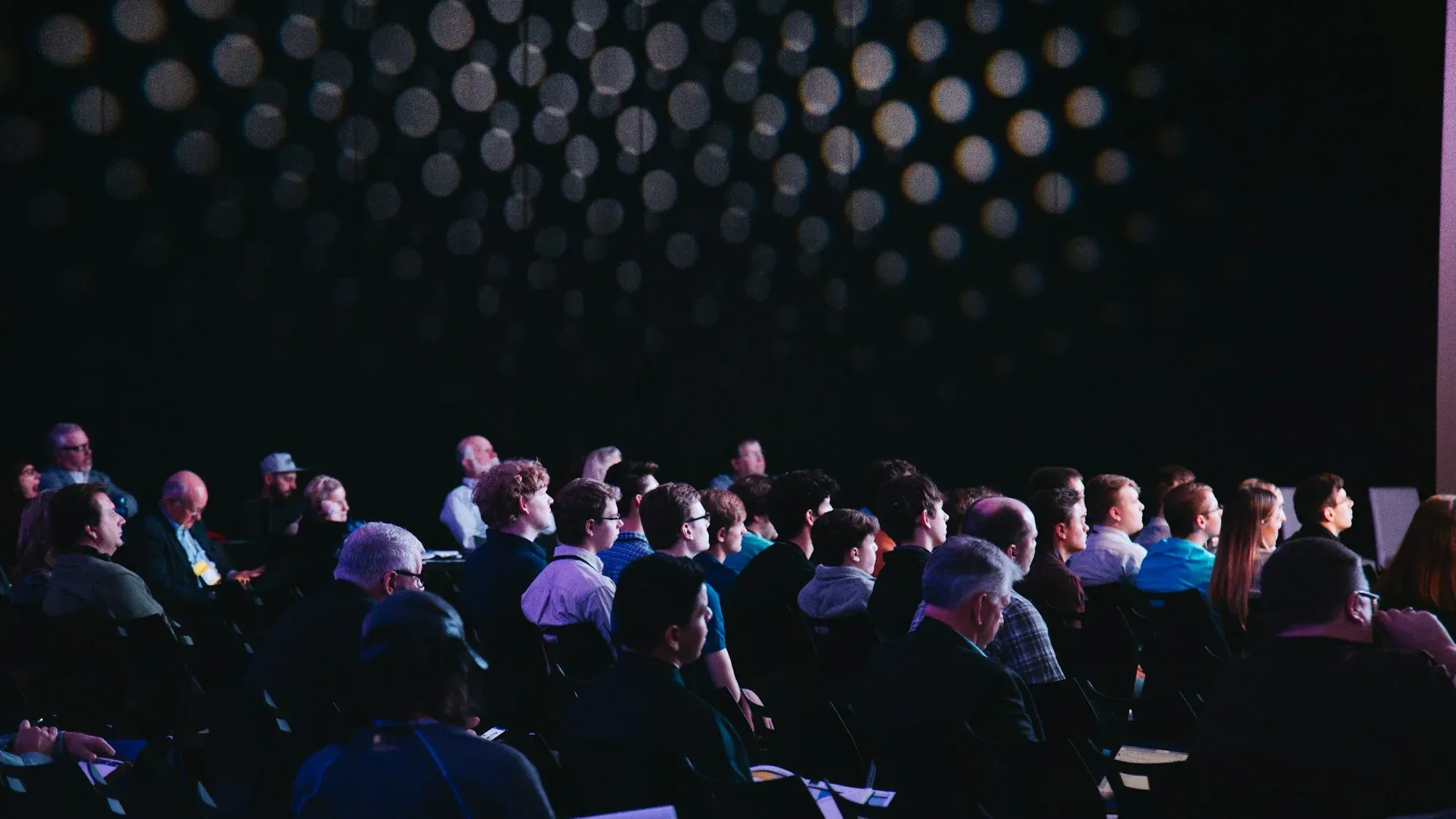 Large audience seated in a dark conference hall facing the stage